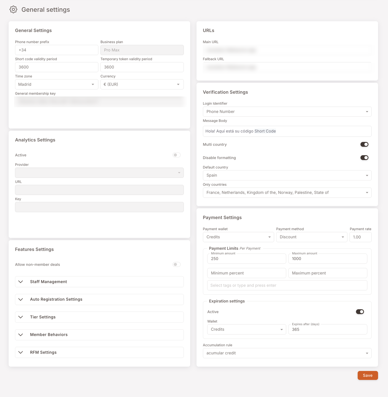 La página de Configuración general, organizada en dos columnas de tarjetas. Columna izquierda: Configuración general (prefijo del número de teléfono +34, plan de negocio, períodos de validez de código corto y token temporal, zona horaria Madrid, moneda € EUR, clave general de membresía); Configuración de analíticas (interruptor Activo, Proveedor, URL, Clave); Configuración de funciones (interruptor Permitir ofertas para no-miembros más acordeones plegables — Gestión de personal, Configuración de auto-registro, Configuración de niveles, Comportamientos del miembro, Configuración RFM). Columna derecha: URLs (URL principal, URL de respaldo); Configuración de verificación (Identificador de inicio de sesión, Cuerpo del mensaje, Multipaís, Desactivar formato, País por defecto, Solo países); Configuración de pagos (Cartera de pago Créditos, Método de pago Descuento, Tasa de pago, Límites de pago, Configuración de caducidad, Regla de acumulación). Un botón Guardar abajo a la derecha.