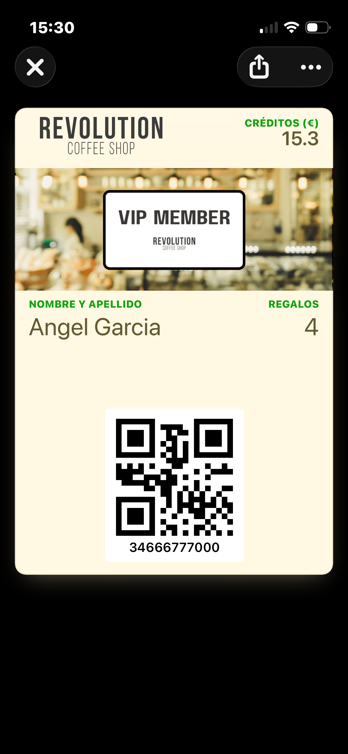 El Wallet Pass de vista condicional en iPhone para un miembro etiquetado Nivel_VIP — tarjeta crema con la marca denominativa Revolution Coffee Shop arriba a la izquierda, Créditos (€) 15.3 arriba a la derecha, una imagen strip VIP MEMBER, colores de etiqueta verdes y texto marrón oscuro, QR del miembro e ID en la parte inferior. Mismos datos que la tarjeta por defecto, solo un tratamiento visual diferente