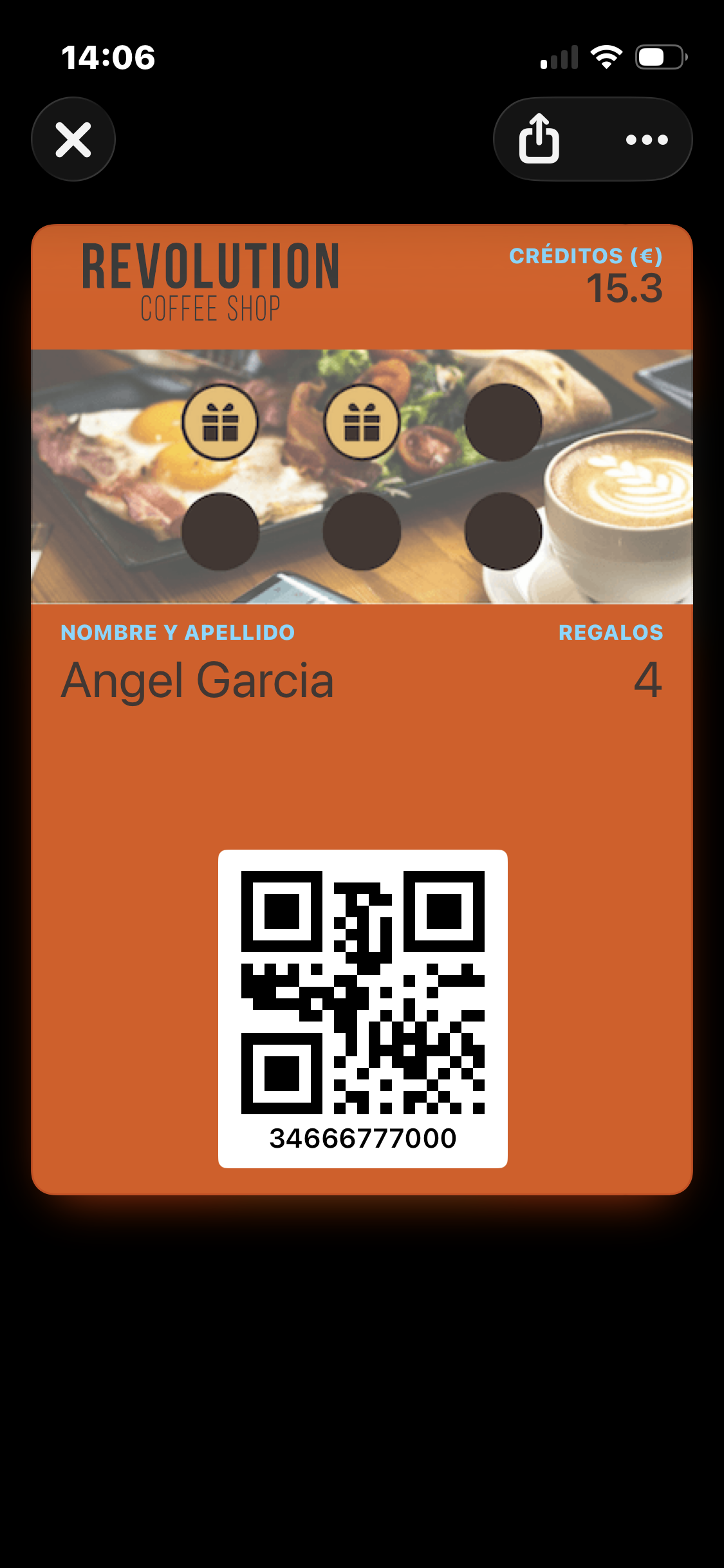El Wallet Pass abierto en un iPhone — tarjeta naranja con la marca denominativa en la esquina superior izquierda, "Créditos (€) 15.3" en la esquina superior derecha, una imagen banner de desayuno con dos sellos ganados (iconos de regalo) y tres no ganados (círculos vacíos), nombre del miembro y conteo de regalos sobre un código QR del miembro, y el número de teléfono del miembro debajo del QR